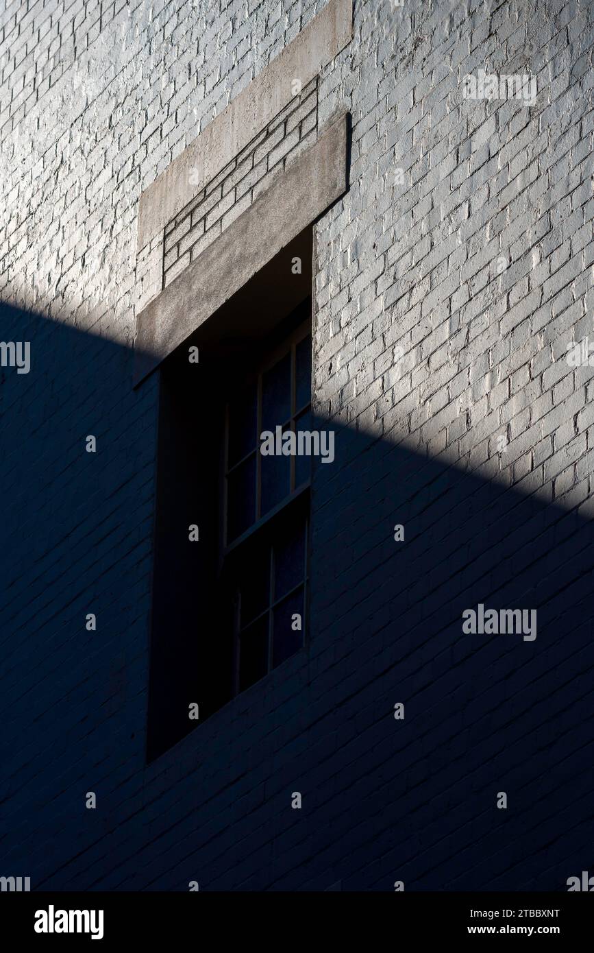 Ein altes Backsteingebäude und Fenster, alle grau lackiert, wird von einer diagonalen Linie bedeckt, die von Schatten und Licht in Sydney, Australien, gebildet wird Stockfoto