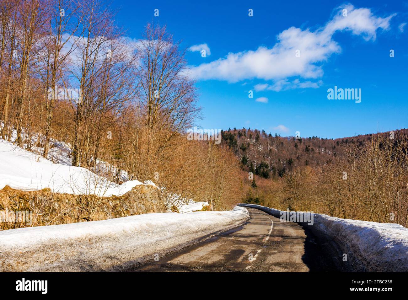 Die alte Straße führt durch schneebedeckte, bewaldete Hügel. Bergige Winterlandschaft an einem sonnigen Tag unter blauem Himmel mit Wolken Stockfoto