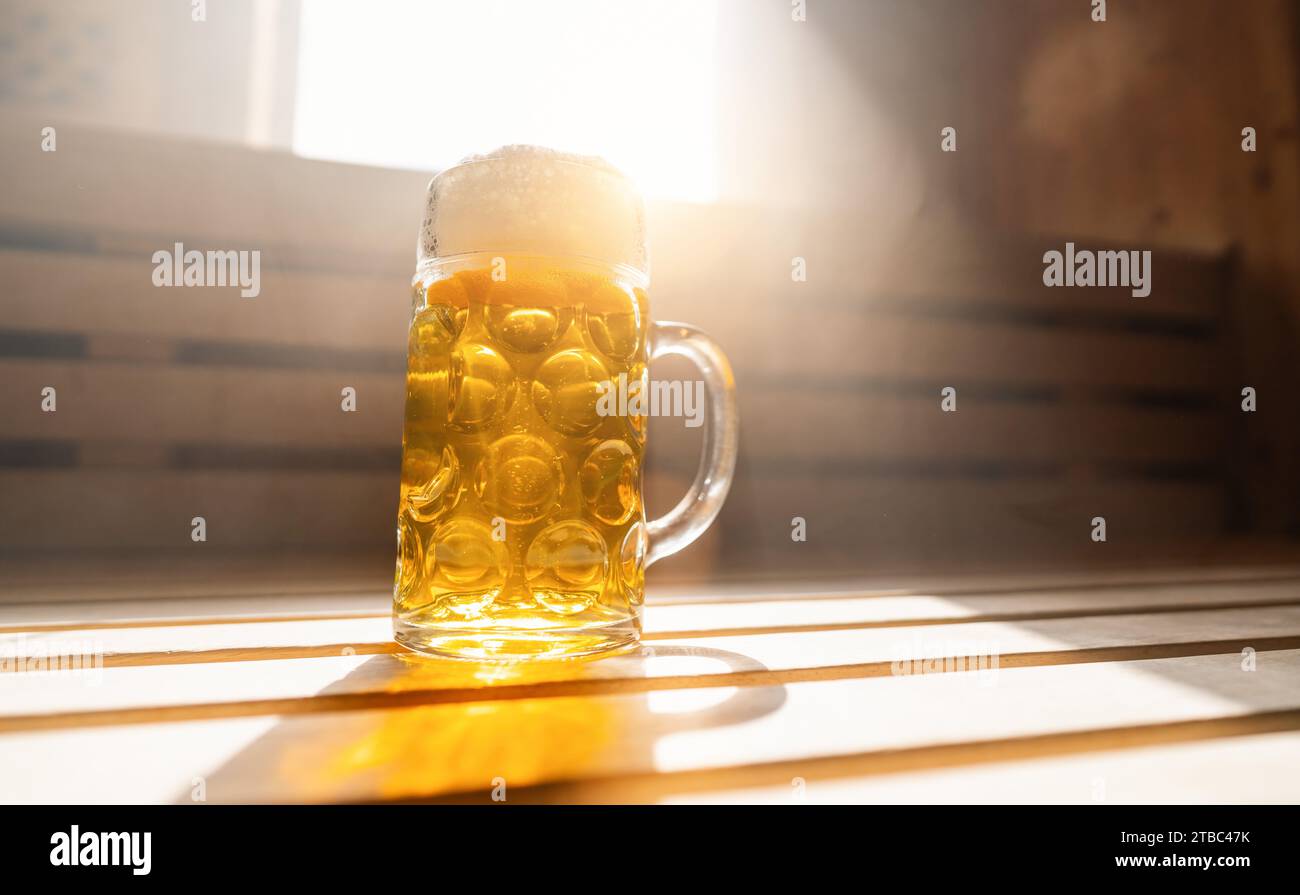 Bierkrug mit schäumendem Bier ruht auf einem Felsvorsprung in einer finnischen Sauna und fängt Sonnenlicht ein. Bild des Spa- und Wellnesskonzepts Stockfoto