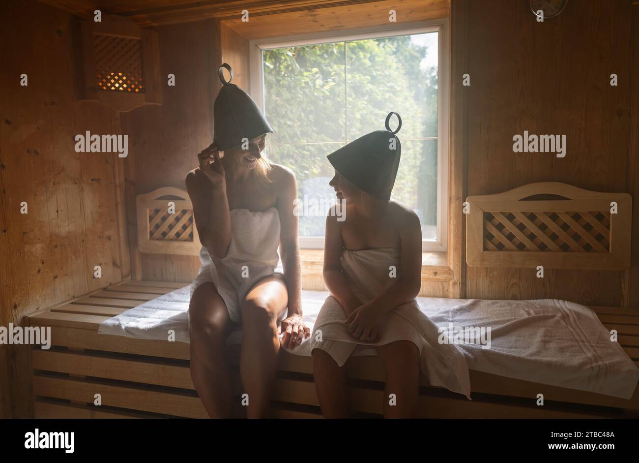 Mutter und Tochter in einer Sauna, beide tragen Filzhüte und unterhalten sich in einem Wellnesshotel Stockfoto