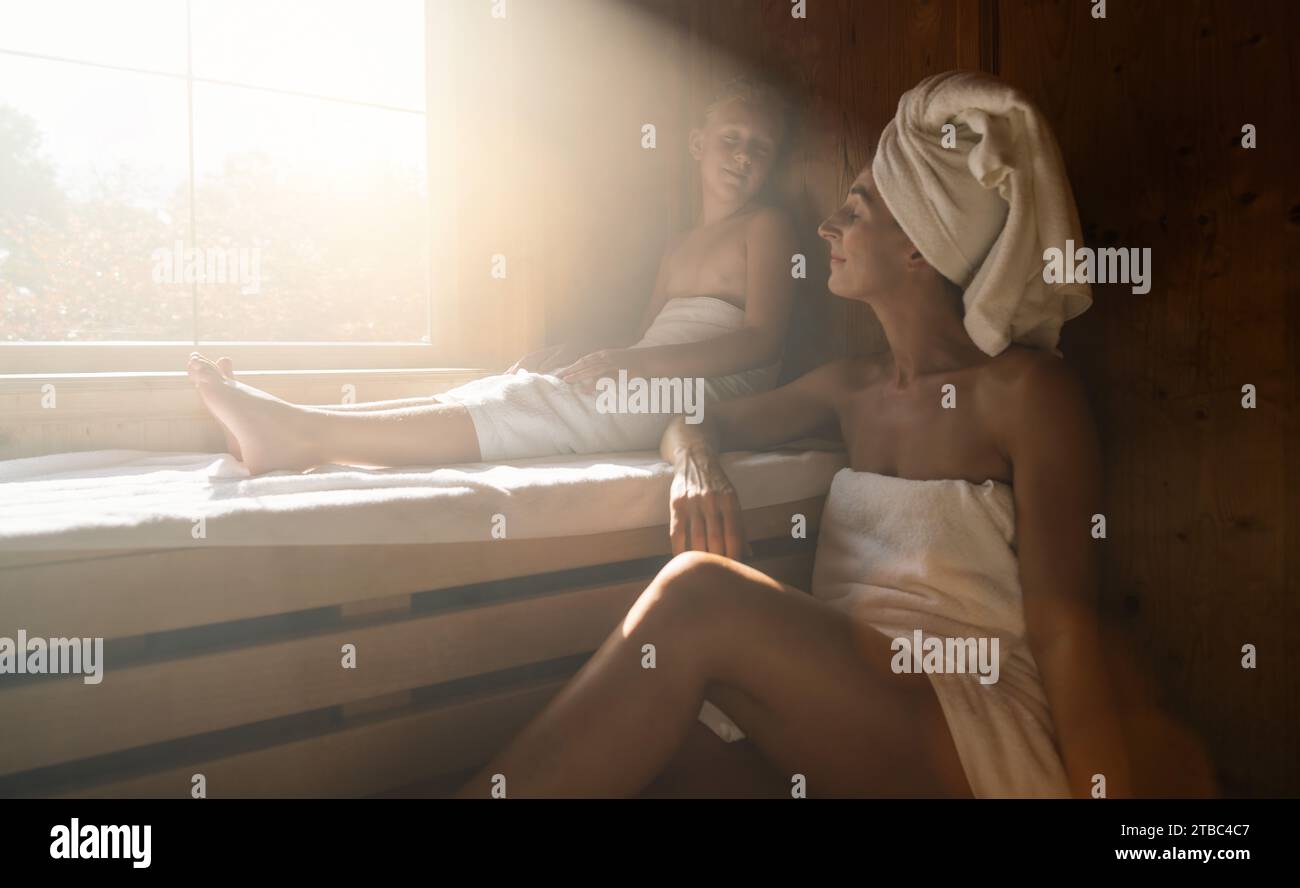 Mutter und Tochter in einer finnischen Sauna, entspannen und genießen die Wärme des sonnendurchfluteten Fensters neben dem Spa Resort Stockfoto