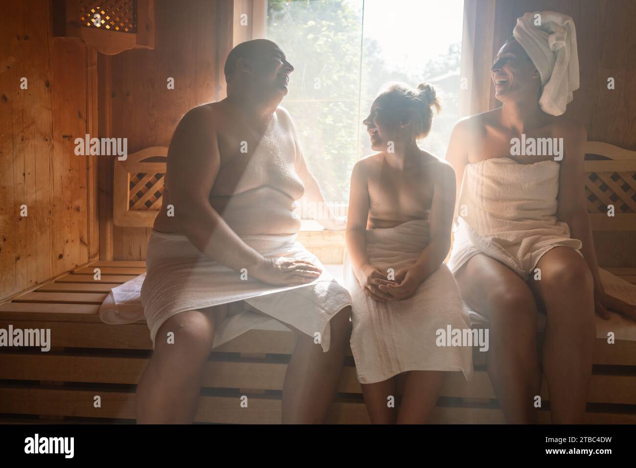 Familie in einer finnischen Sauna, Mann links, Frau mit Handtuch auf dem Kopf rechts, Kind im Zentrum im Wellnesshotel Stockfoto