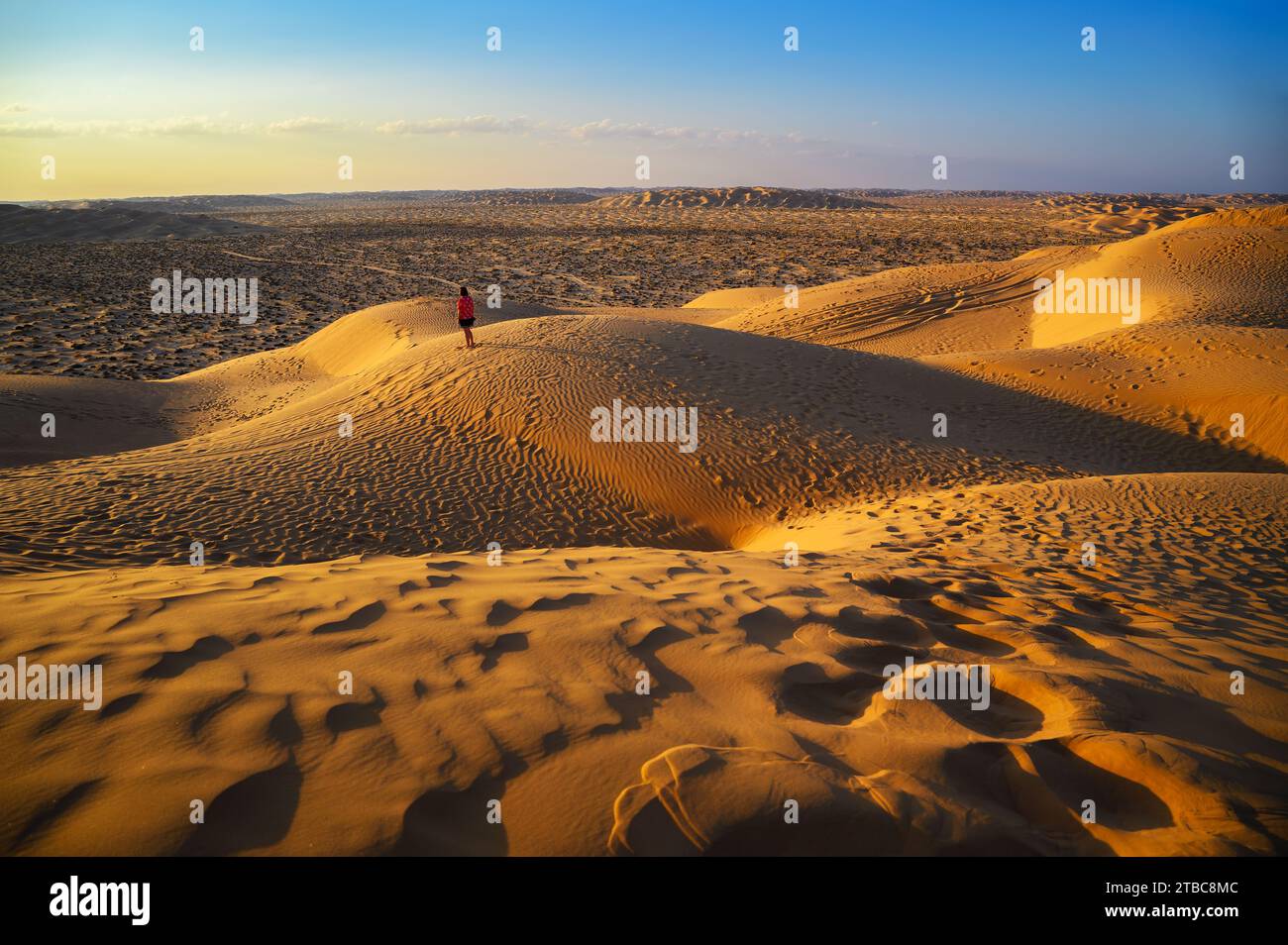 Frau, die den Sonnenuntergang über den Sanddünen der Arabischen Wüste in Oman beobachtet Stockfoto