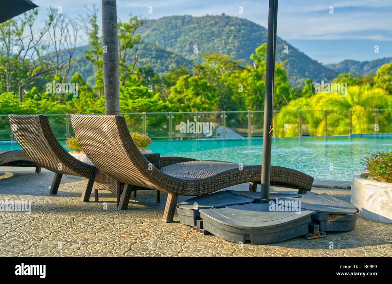 Leere zwei Korbliege neben einem Swimmingpool eines Resorts, Morgenlicht, Hintergrund von Bäumen, Berg und Himmel. Stockfoto