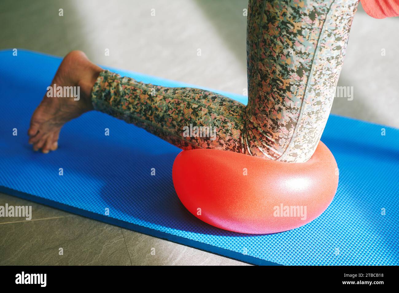 Reife Frau übt während des Pilates-Trainings eine Balance, wobei sie einen weichen Ball für das Knie verwendet Stockfoto