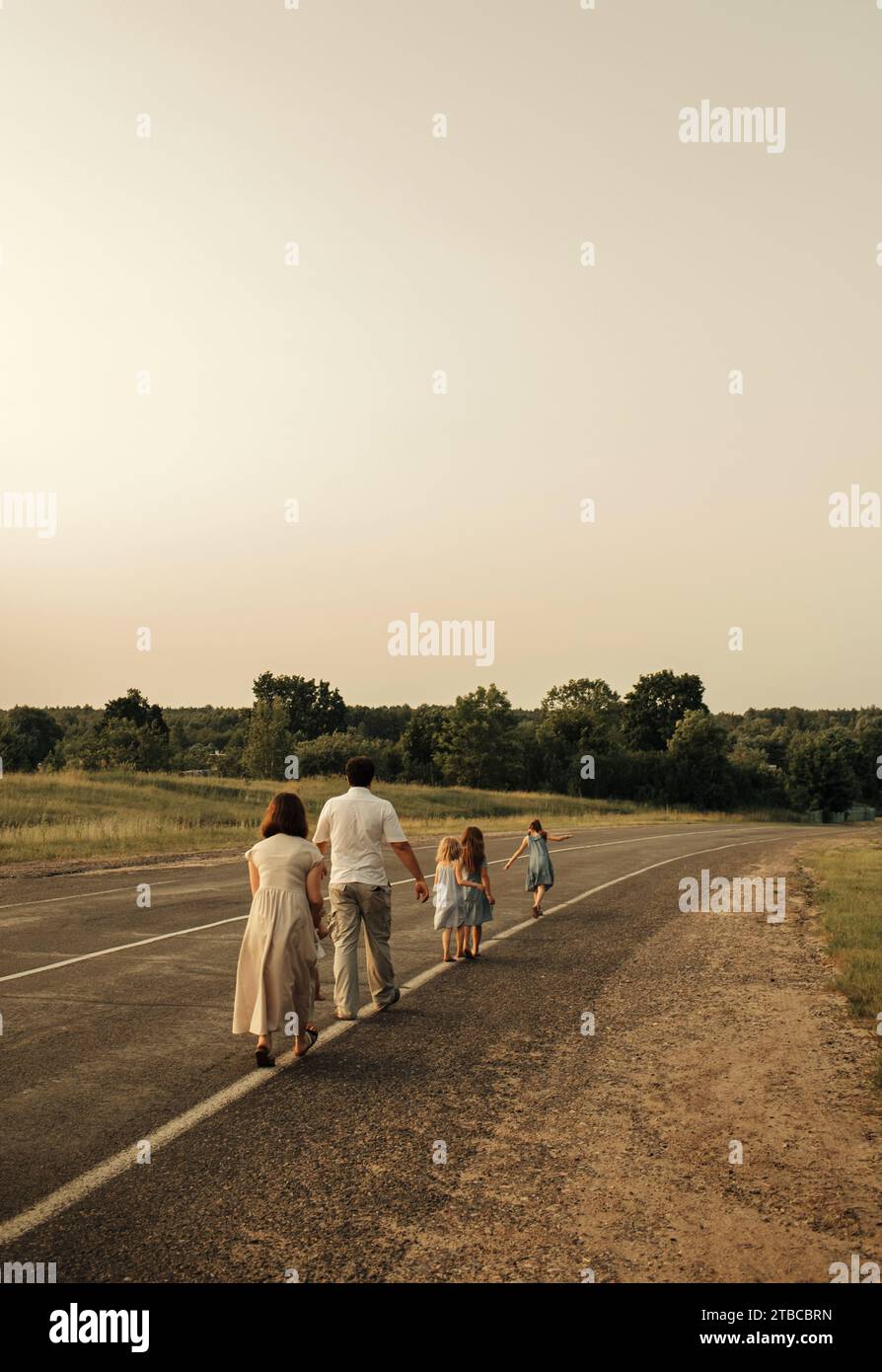 Mom, Dad und Töchter laufen einer nach dem anderen auf einer Landstraße entlang des Waldes. Eine glückliche Familie Stockfoto