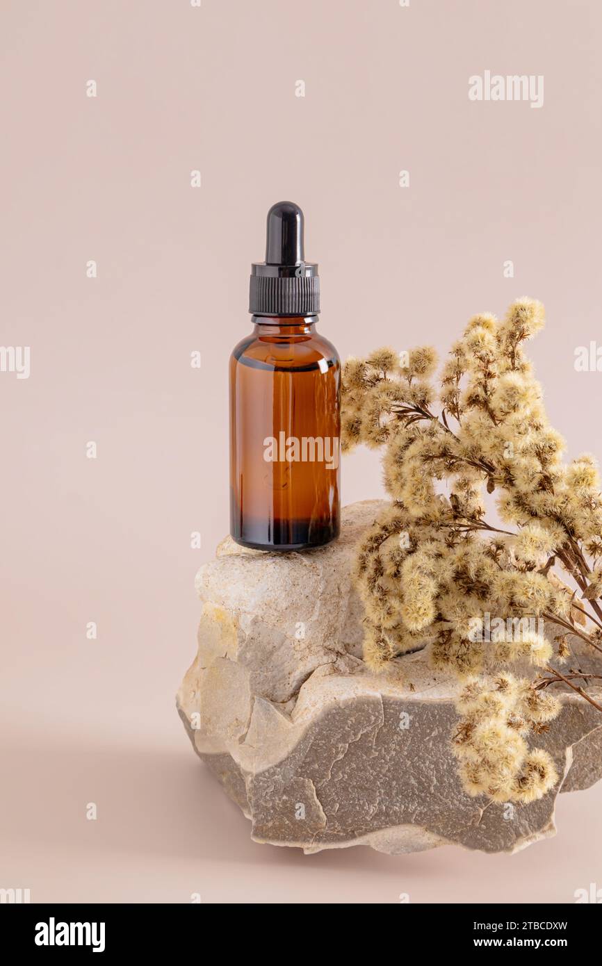 Ein kosmetisches Produkt in einer Glasflasche mit Tropfer steht auf einem beigen Naturstein. Verpackung. Branding-Layout. Vertikale Vorderansicht Stockfoto