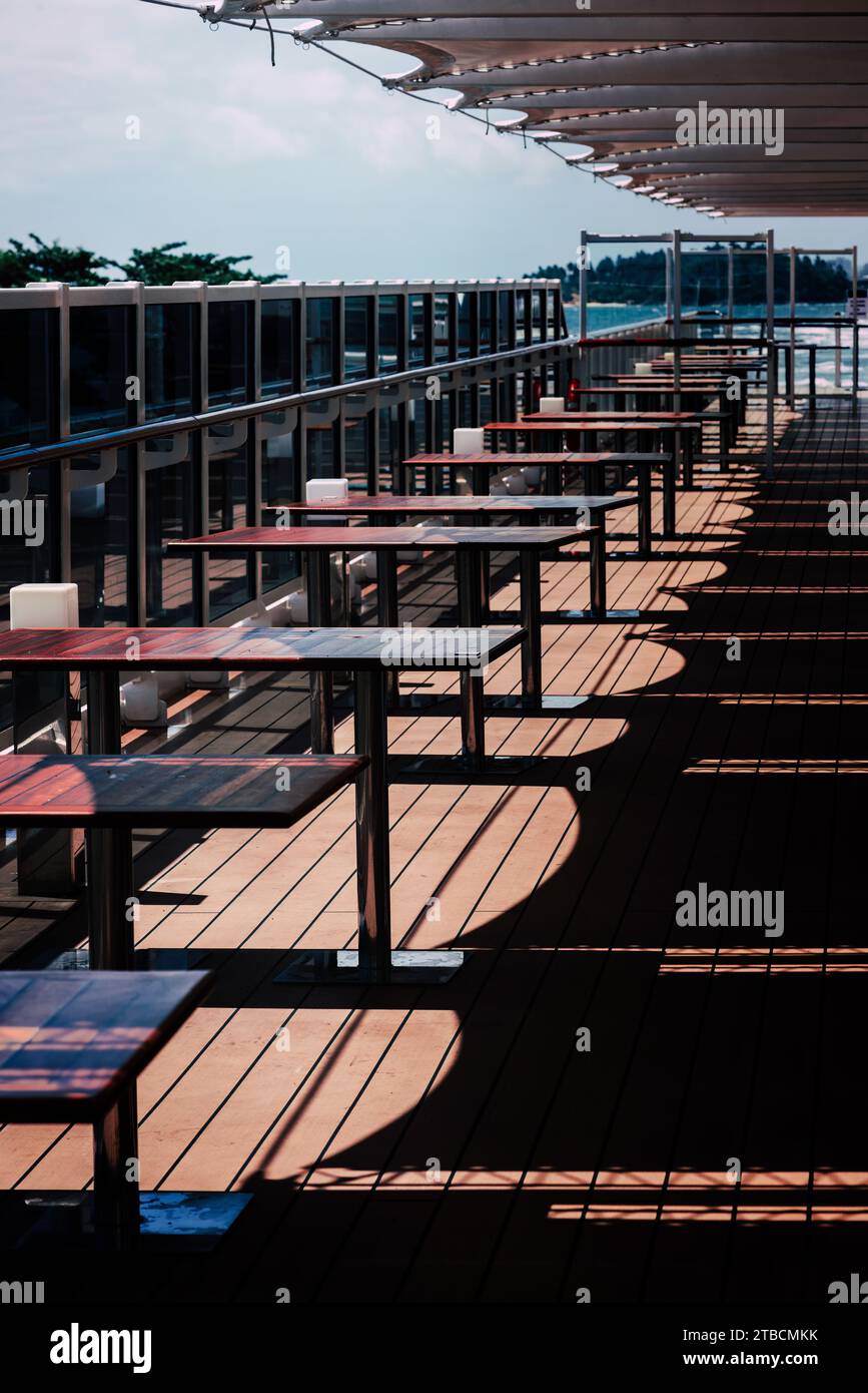 Tische auf einem Deck mit Geländer auf einem Kreuzfahrtschiff in tropischer Umgebung Stockfoto