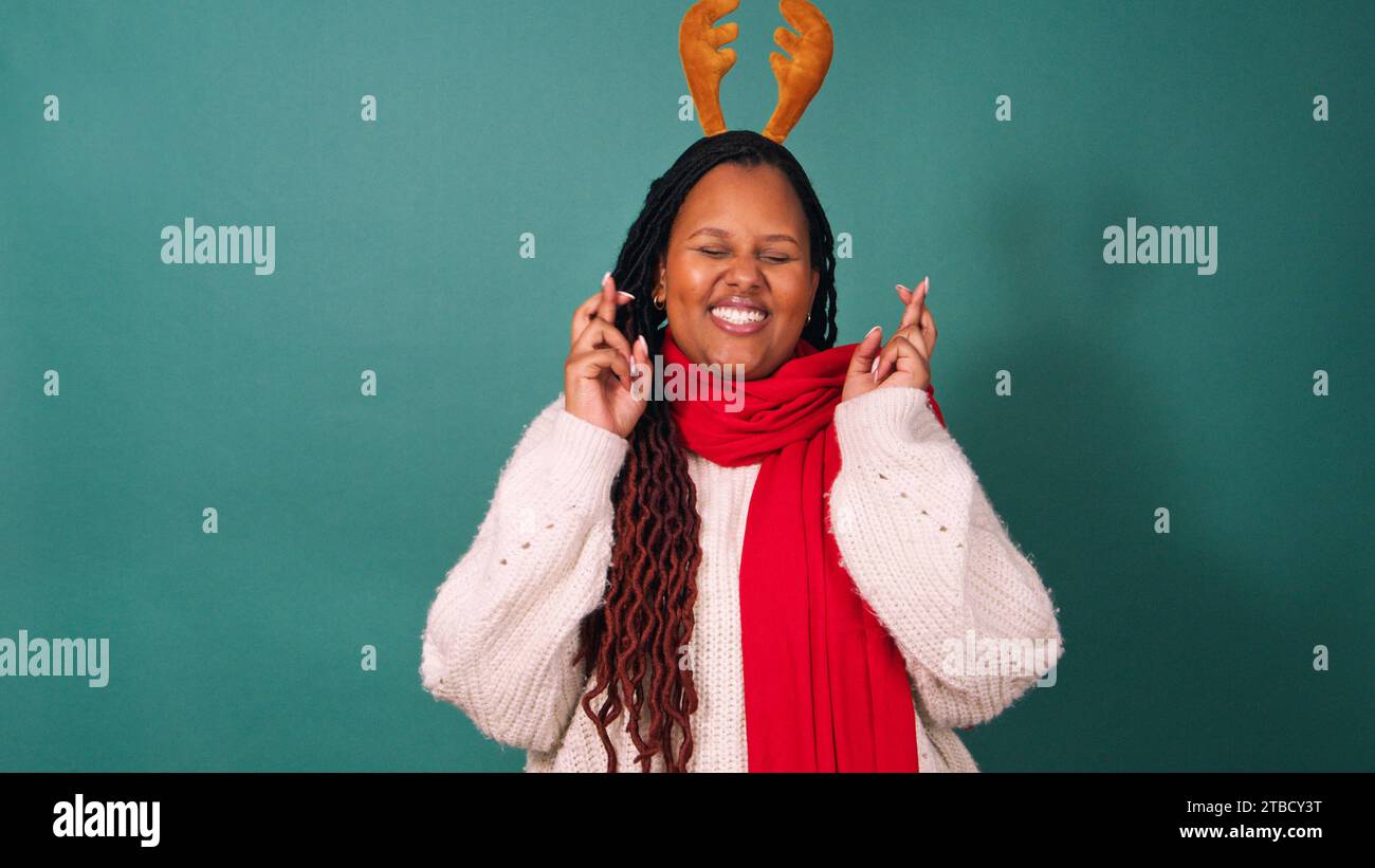 Schöne junge Frau mit gekreuzten Fingern, die Weihnachtswünsche wünscht und hofft Stockfoto