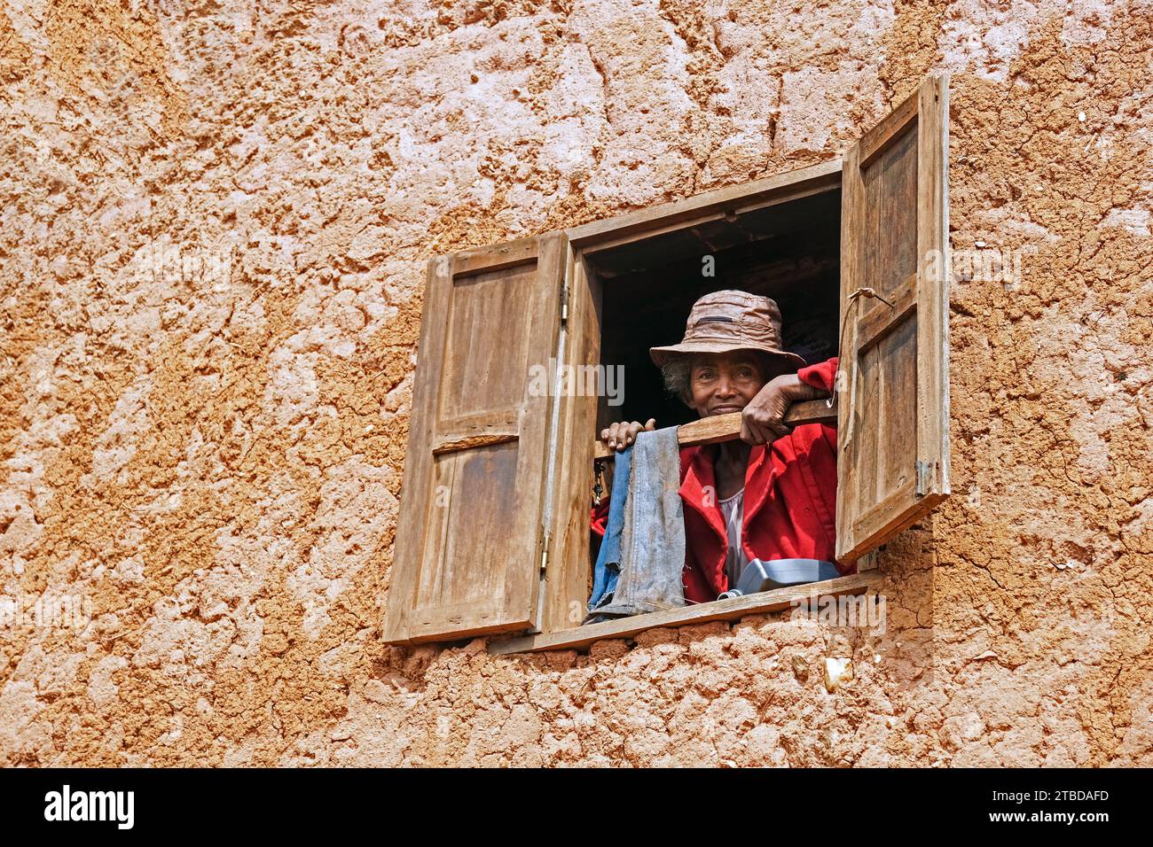 Ältere madagassische Frau, die vom Fenster aus in einem zweistöckigen Lehmhaus im Ambositra-Viertel, Amoron'i Mania-Region, Zentralmadagaskar, Afrika, blickt Stockfoto