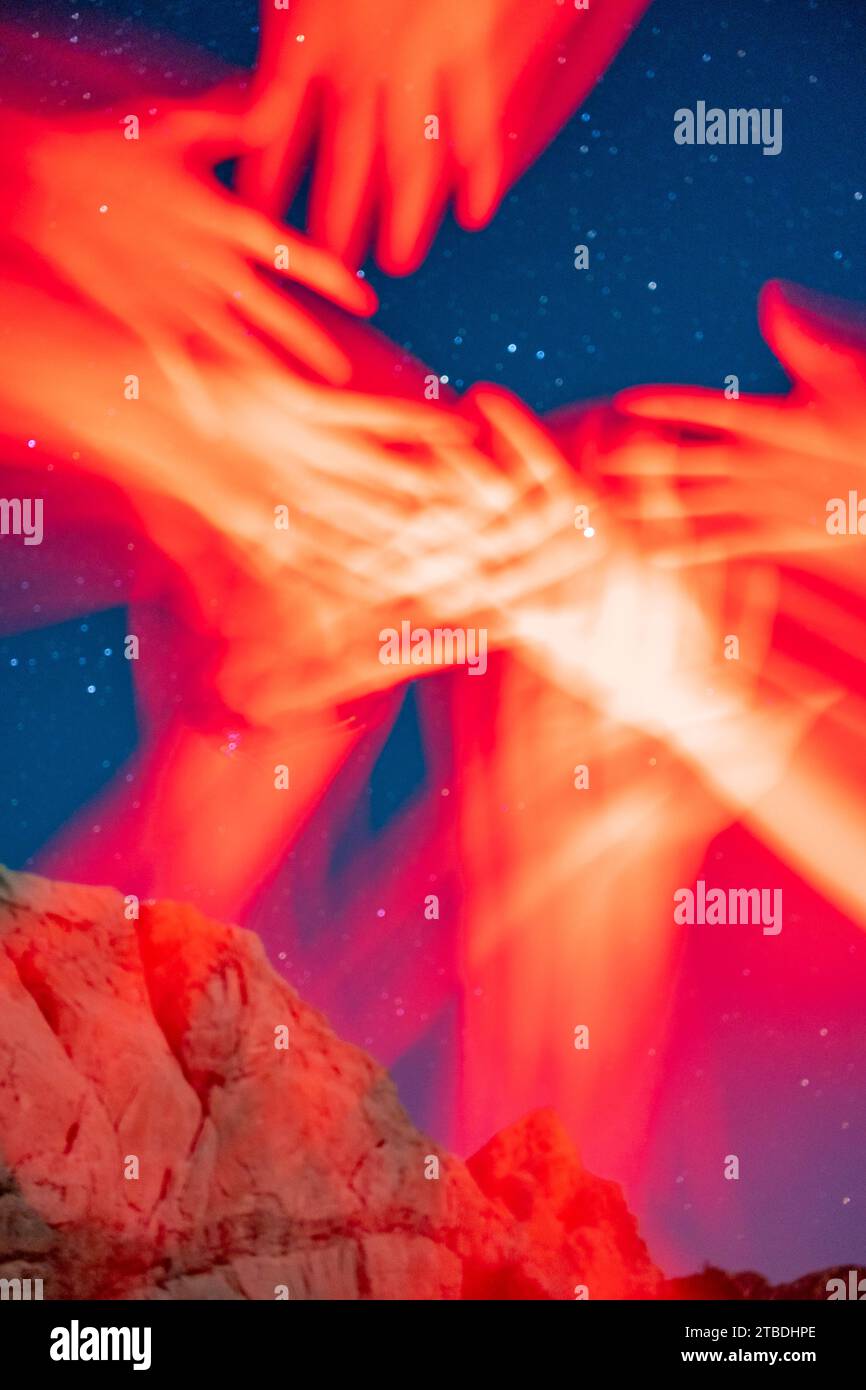 Arme, die im roten Licht greifen und winken, aufgenommen mit einer sternenklaren Wüstenlandschaft im Hintergrund. Stockfoto