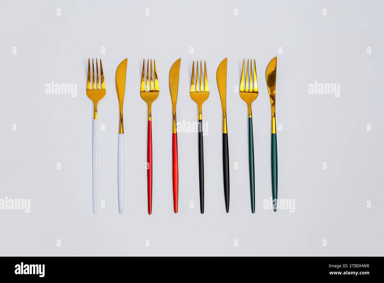 Goldene Gabeln und Messer mit bunten Griffen auf weißem Hintergrund Stockfoto