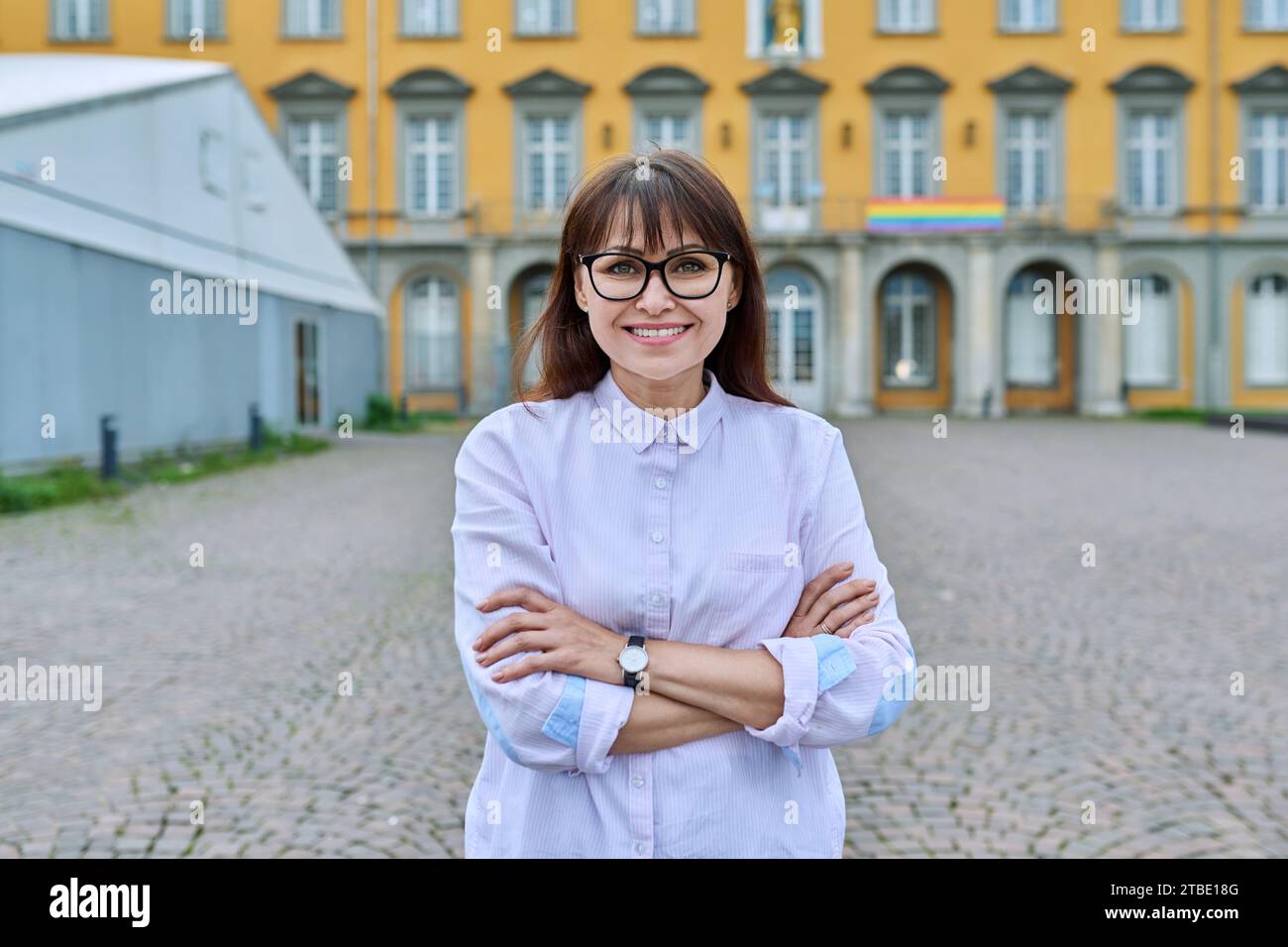 Lehrerin mittleren Alters posiert vor dem Hintergrund des Bildungsaufbaus Stockfoto