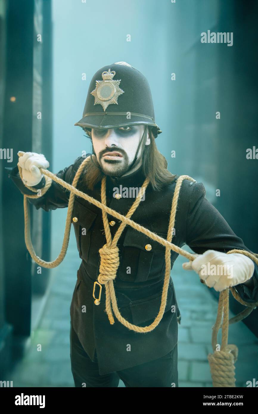 Ein Porträt eines männlichen Cosplayer bei einem Comic-Concept-Event in einer gruseligen Uniform der britischen Polizei mit weiß bemaltem Gesicht und Hangmans-Schlinge in der Altstadt von London i Stockfoto