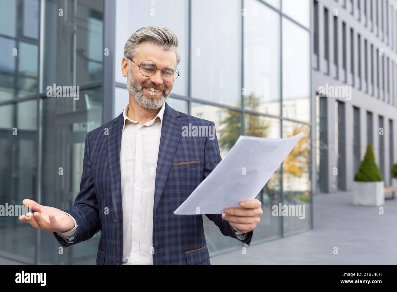 Zufriedener Geschäftsmann im Anzug, der Geschäftspapiere hält, vor dem Büro auf der Straße steht, erfolgreiche Verhandlungen, gute Nachrichten. Stockfoto