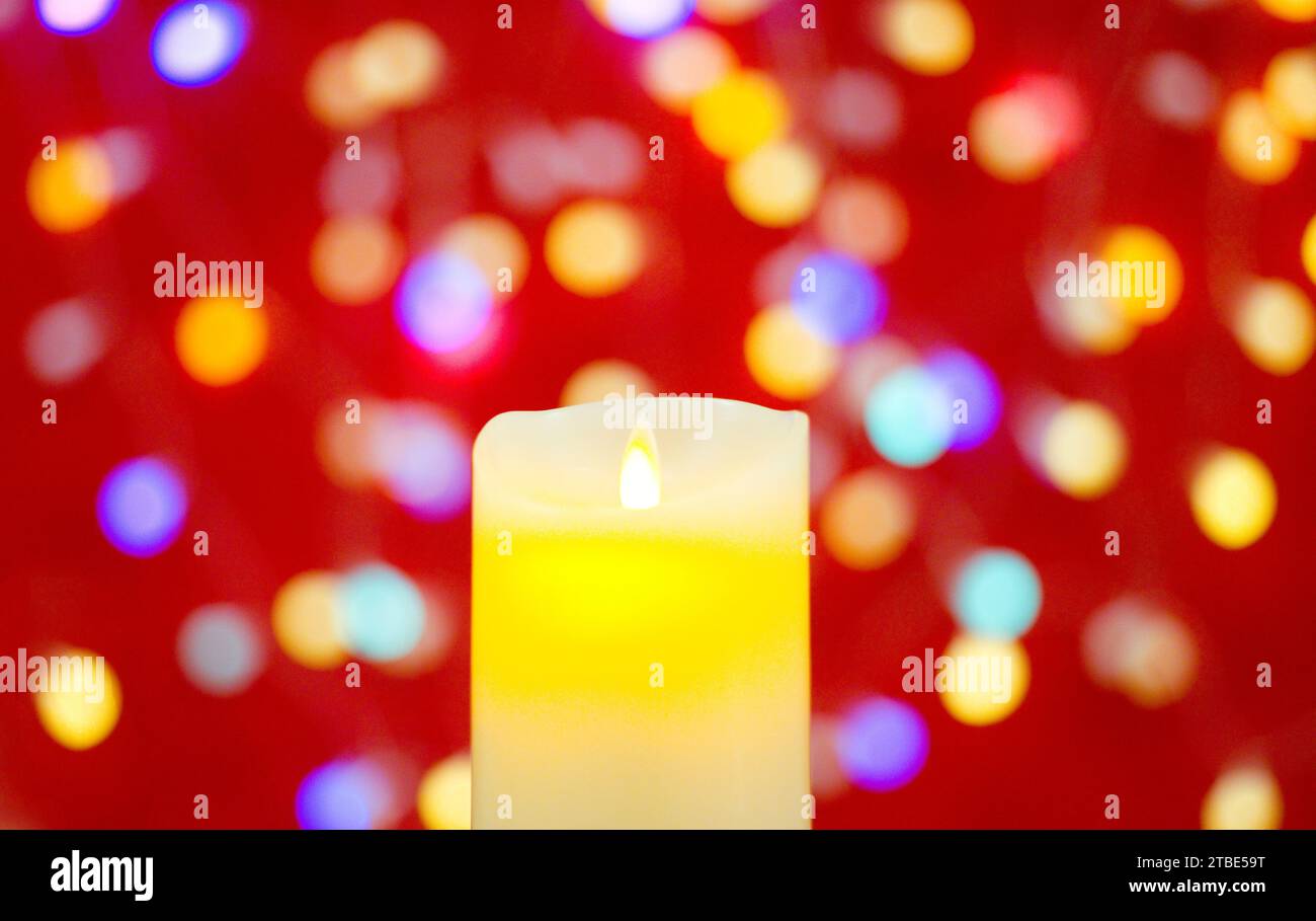 Kerze brennt vor einem unscharfen Hintergrund mit Lichtern auf rotem Hintergrund Stockfoto