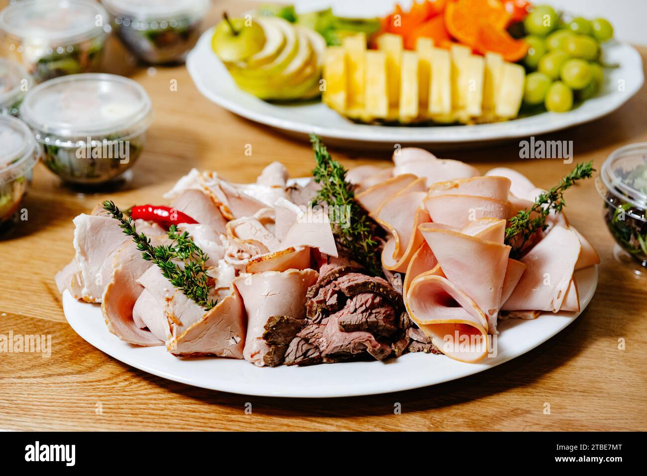 Eine Auswahl an aufgeschnittenem Aufschnitt, serviert auf einer Platte, begleitet von Kräutern und Chili-Paprika, frische Obstplatte auf einem Hintergrund. Stockfoto