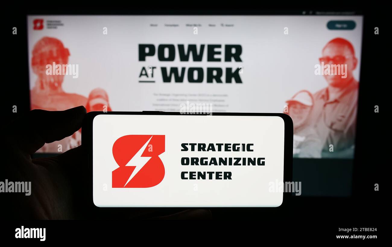 Person mit Handy mit Logo der gewerkschaftskoalition Strategic Organizing Center (SOC) vor der Webseite. Schwerpunkt auf dem Display des Telefons. Stockfoto