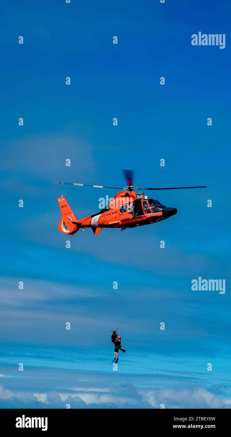 Zwei Rettungsschwimmer hängen an einem H-65 von der Air Station Barbers Point vor der Nordküste von Oahu, Hawaii. Die Air Station Barbers Point führte am 5. Dezember 2023 ein Rettungsschwimmer-Training durch, mit einem unter Vertrag stehenden Schiff der Küstenwache. Stockfoto