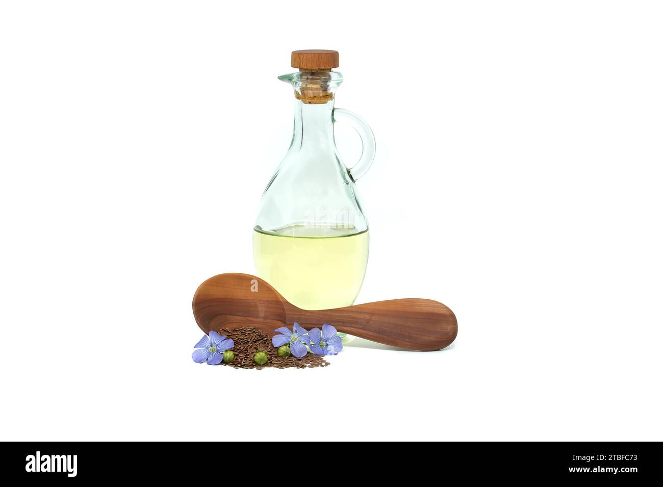 Holzlöffel gefüllt mit kleinen braunen Leinsamen und einer blauen Leinpflanze blüht neben Leinöl in Glasdekanter isoliert auf weißem Hintergrund Stockfoto