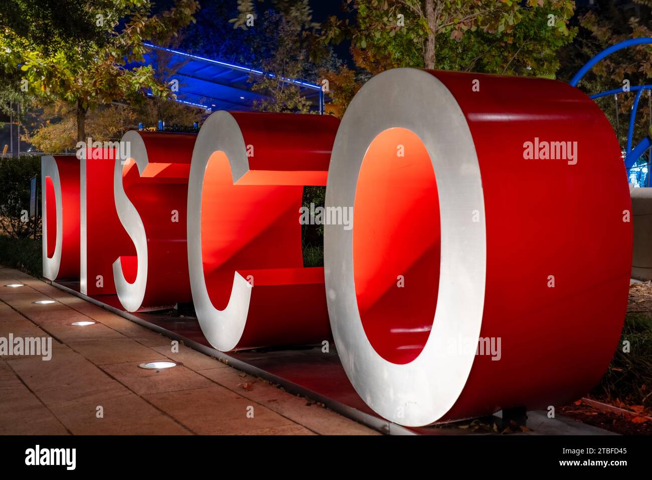 Rote und graue dreidimensionale 3D-Buchstaben, die das Wort DISCO bilden, mit einem abendlichen Outdoor-Hintergrund. Stockfoto