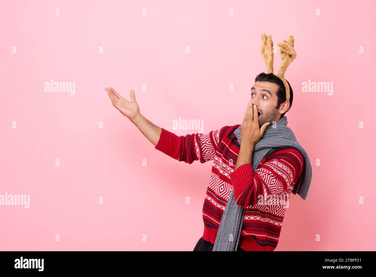 Das Weihnachts-Studio hat Porträt eines überraschten Kaukasiers mit Pullover und einem schicken Rentier-Stirnband aufgenommen, der die Hand in den Kopierraum in rosafarbener Farbe isol bringt Stockfoto