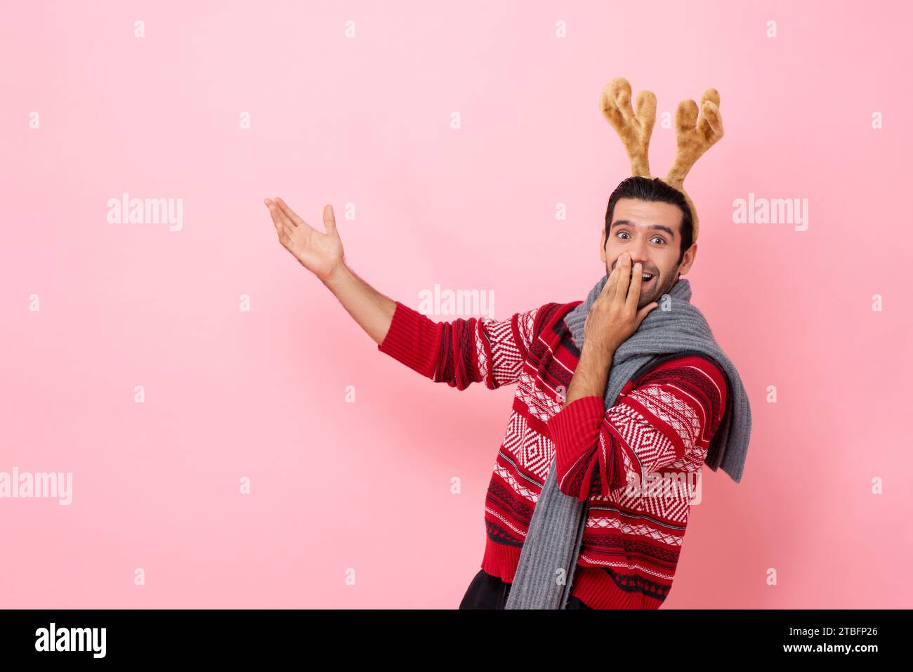 Das Weihnachtsstudio hat ein Porträt eines schockierten Kaukasiers mit Pullover und einem schicken Rentier-Stirnband aufgenommen, der die Hand in den Kopierraum in rosa Isolat streckt Stockfoto