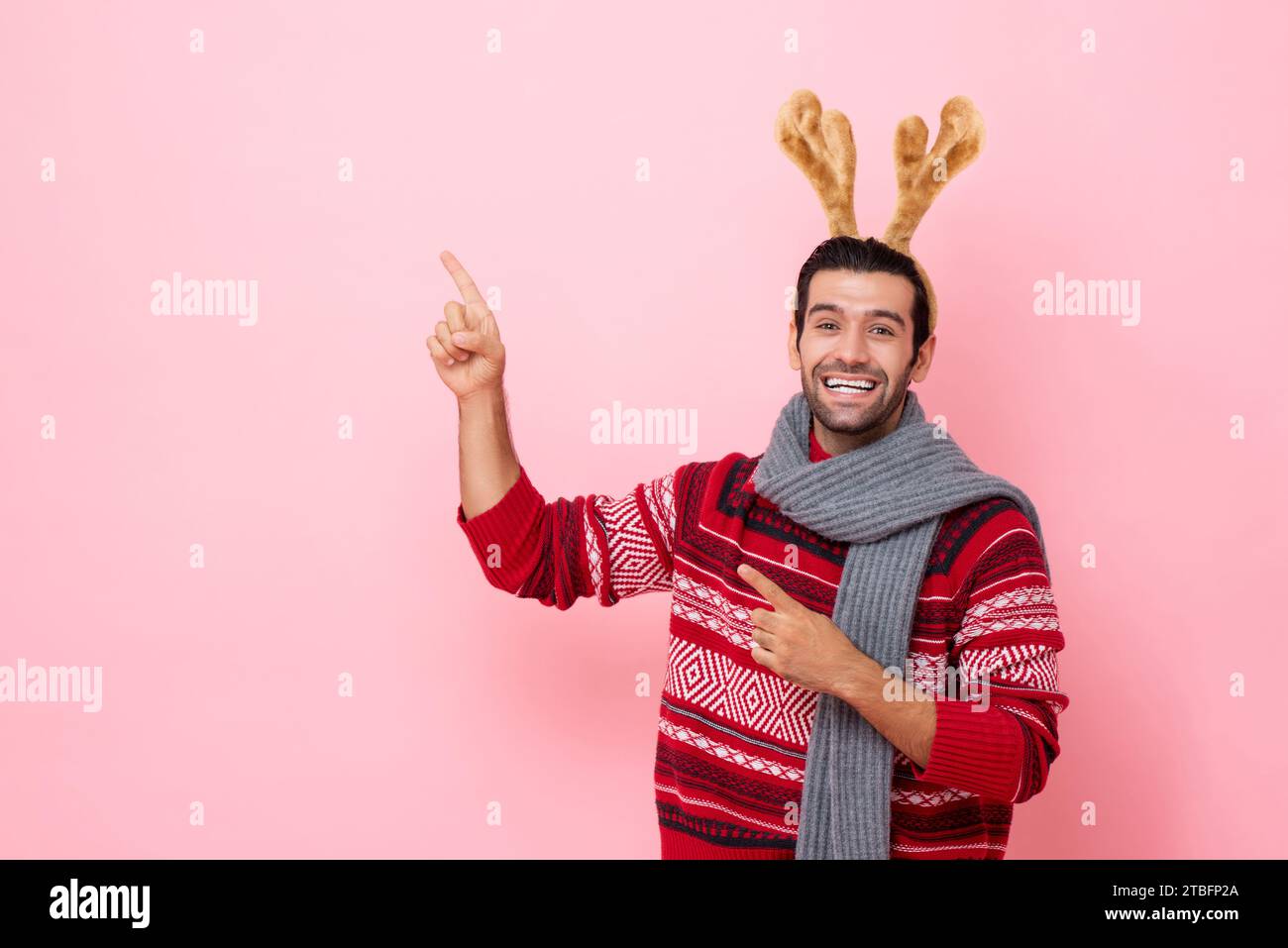 Das Weihnachts-Studio hat Porträt eines Kaukasiers mit Pullover und einem schicken Rentier-Stirnband aufgenommen, der die Hand in den Kopierraum in rosafarbenem, isoliertem Hintergrund zeigt Stockfoto