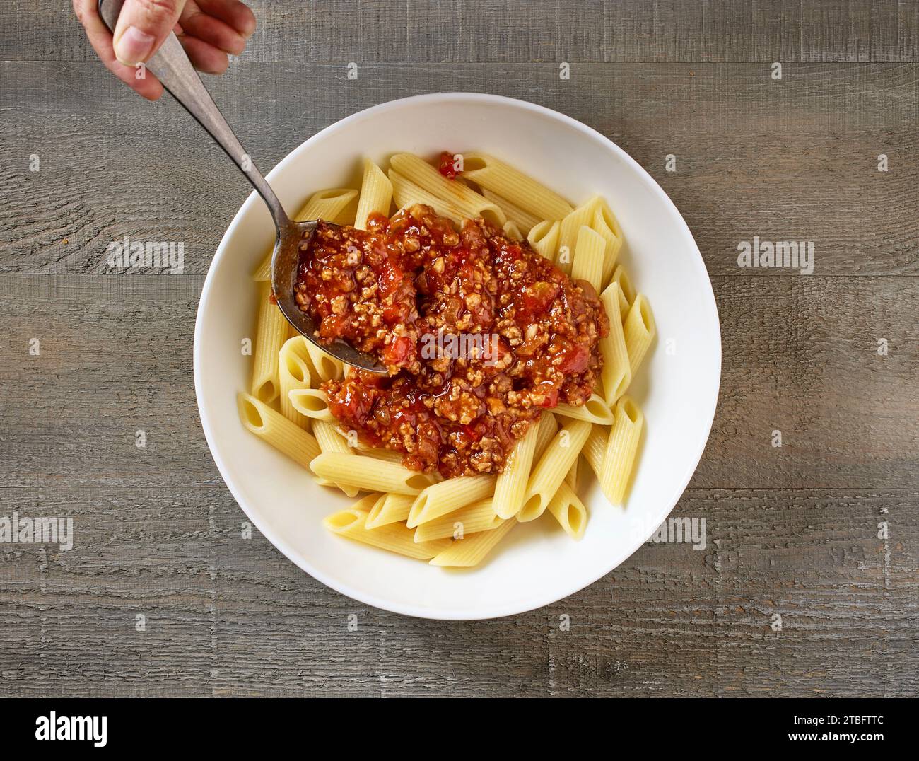 bolognese-Sauce wird in eine Schüssel Pasta gegeben, Blick von oben Stockfoto