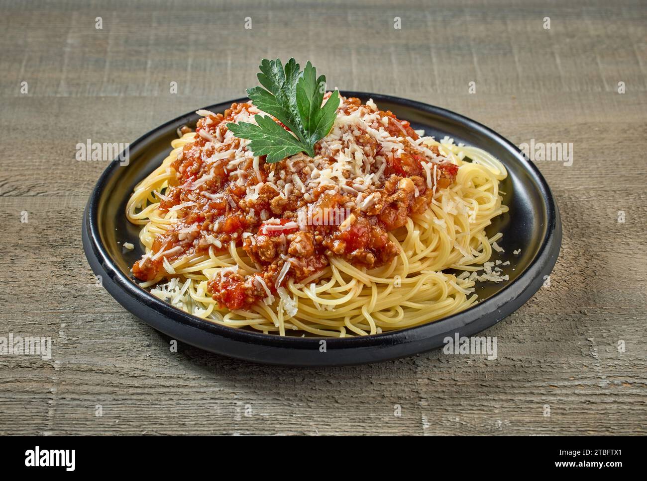 Spaghetti mit Soße Bolognese auf schwarzem Teller auf hölzernem Küchentisch Stockfoto