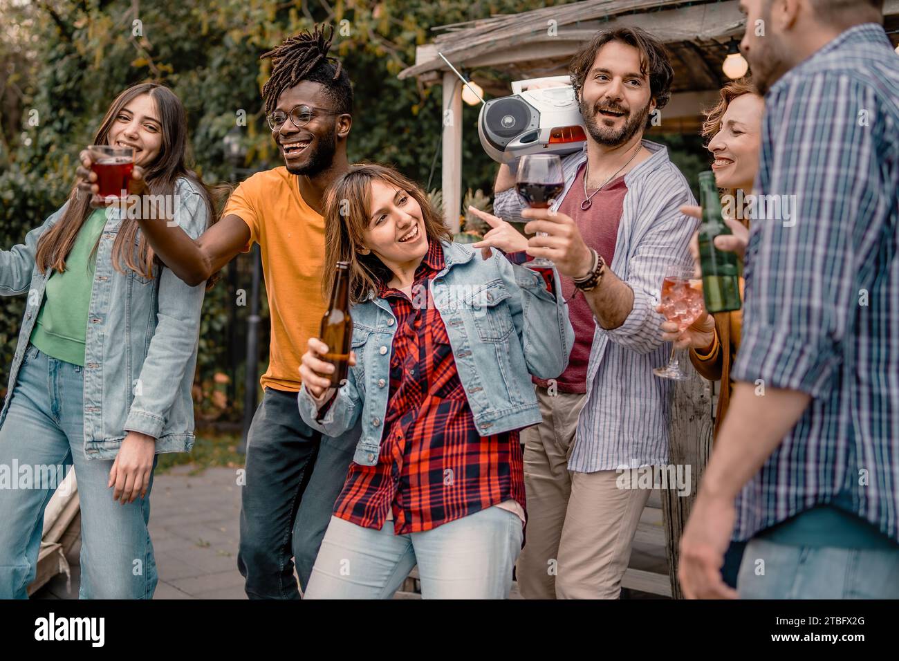 Eine vielfältige Gruppe junger Erwachsener tobt bei einem Treffen im Freien zur Freundschaft und teilt Lachen und Musik aus einer tragbaren Boombox. Stockfoto