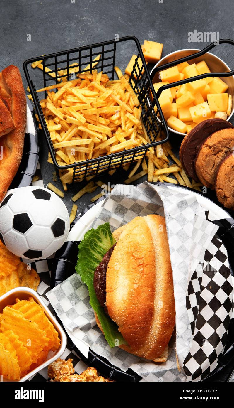 Gesättigte Fette. Fußballzeit. TV-Fernbedienung und Snacks - Chips, Popcorn, Kekse, Käse, Soße, Pommes, Burger, Nüsse. Draufsicht Stockfoto