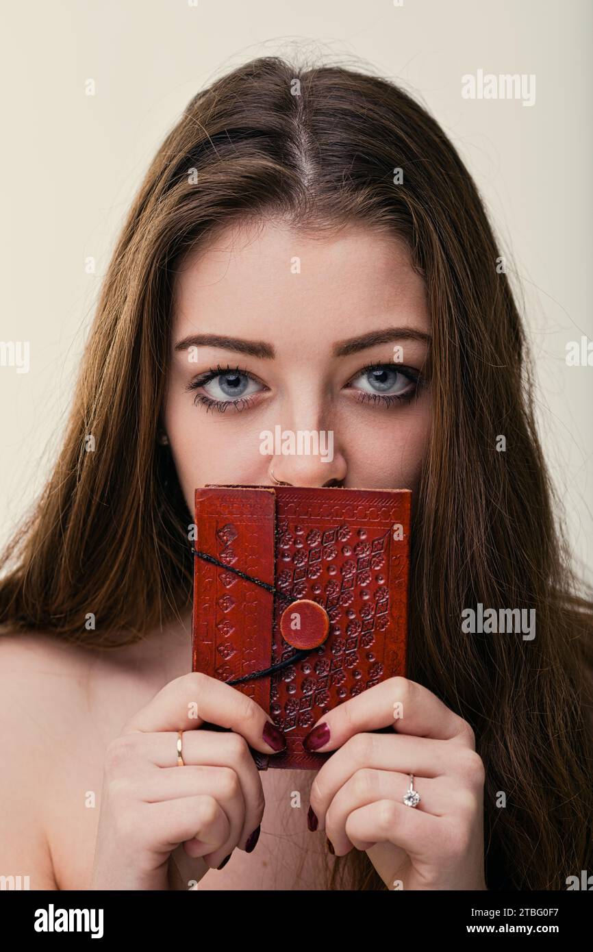 Die rätselhaften Augen einer jungen Frau bezaubern über dem Cover eines strukturierten Tagebuchs und deuten auf unerzählte Geschichten im Inneren hin Stockfoto