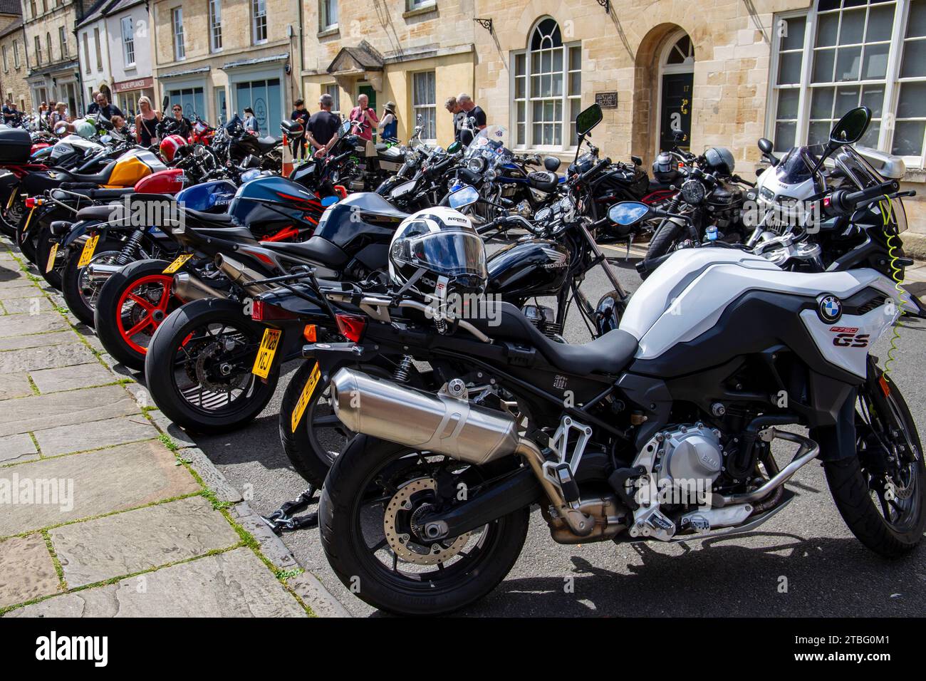 Eine Reihe geparkter Motorräder, darunter ein BMW GS an einem sonnigen Tag mit Menschen, die sich vor historischen Steinhäusern versammelten, treffen sich die Kirche Straße Calne Bike Stockfoto