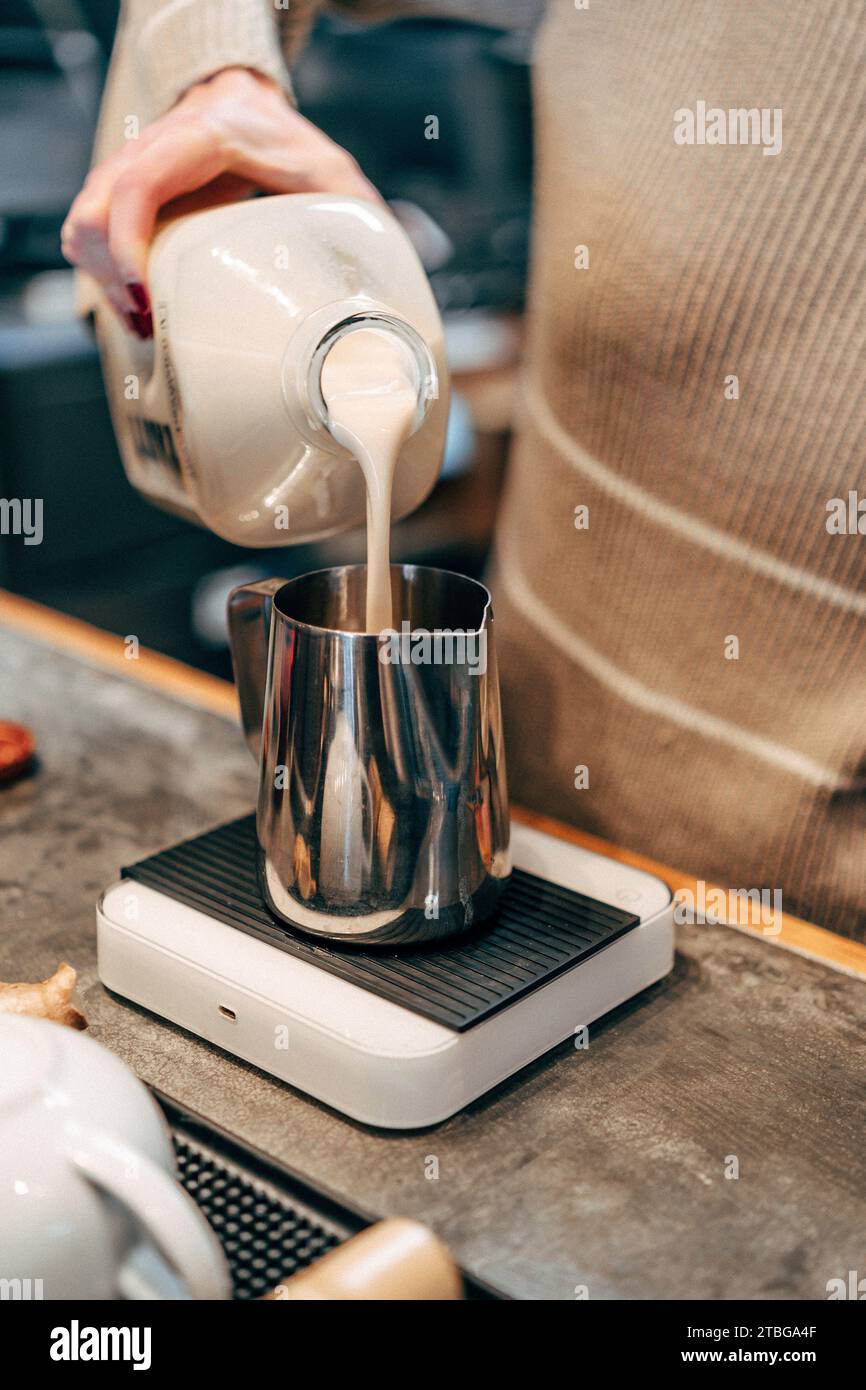 Eine vertikale Aufnahme einer Person, die vorsichtig Milch in einen Metallkrug für Kaffee gießt Stockfoto