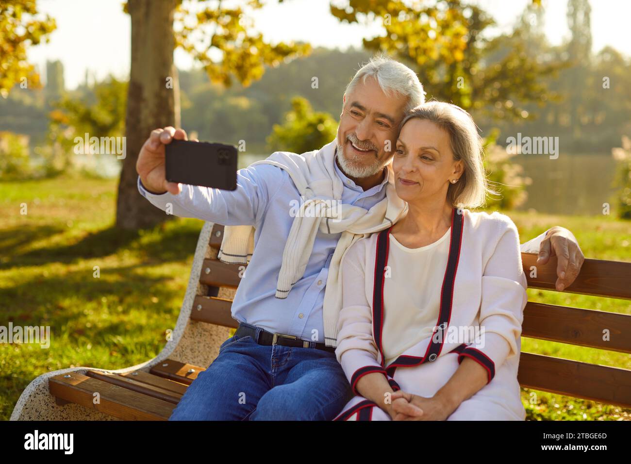 Glückliches Seniorenpaar, das auf einer Bank im grünen Sommerpark sitzt und Selfie am Telefon macht Stockfoto