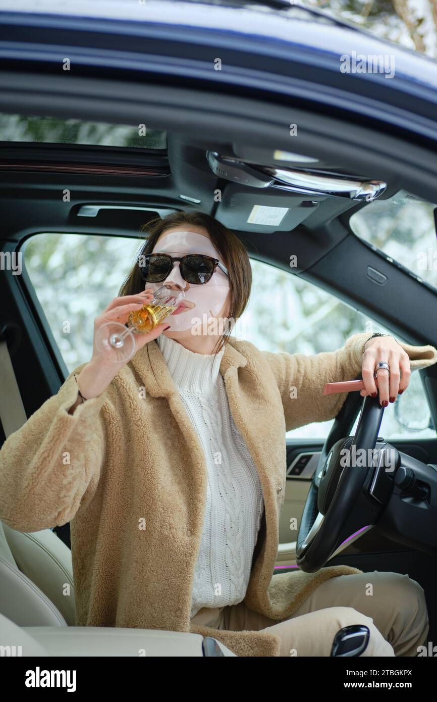 Eine Frau sitzt am Heiligabend auf einer Forststraße in einem Auto fest und trinkt Champagner, während sie auf einen Abschleppwagen wartet. Stockfoto