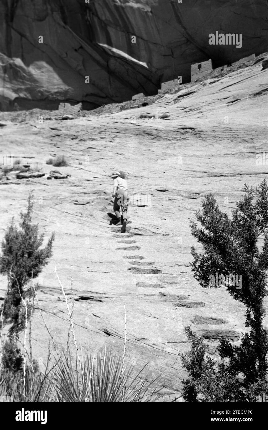 Eine Frau erklimmt die letzten Meter zur Ruinenstätte der Siedlung von Felsenwohnungen Inscription House, die seit 1968 für die Öffentlichkeit gesperrt ist, Arizona 1968. Eine Frau klettert die letzten Meter zur Ruine der Inschrift House Cliff Dwelling Siedlung, die seit 1968 für die Öffentlichkeit gesperrt ist, Arizona 1968. Stockfoto