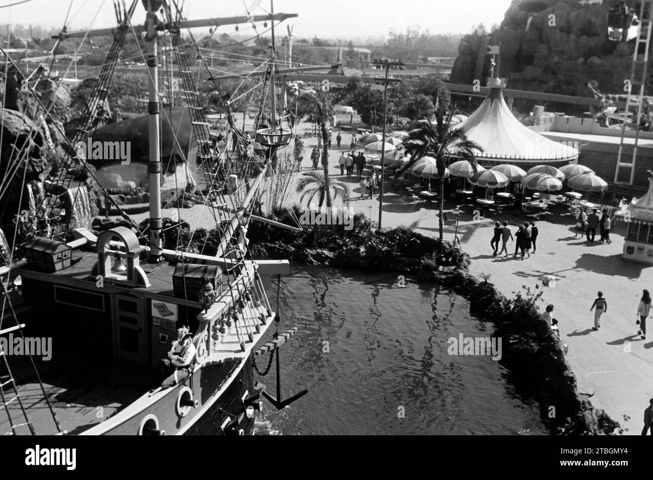 Blick über den Bug des Piratenschiffes Chicken of the Sea im Bereich Fantasyland von Disneyland Anaheim, im Hintergrund ein Pavillon mit Tischen und Schirmen sowie ein Teil des Matterhorn und der Fahrbahn des Monorail, 1962. Blick über den Bug des Chicken of the Sea Piratenschiffs im Fantasyland-Gebiet von Disneyland Anaheim, mit einem Pavillon mit Tischen und Regenschirmen und einem Teil der Matterhorn- und Monorail-Bahn im Hintergrund, 1962. Stockfoto