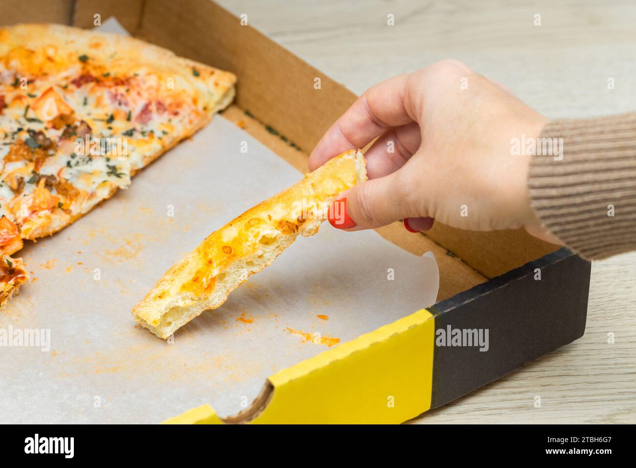 Frau, die trockene Pizzakruste in eine Kiste steckt. Trockene Pizzakruste. Übrig gebliebene Pizza auf dem Tisch Stockfoto