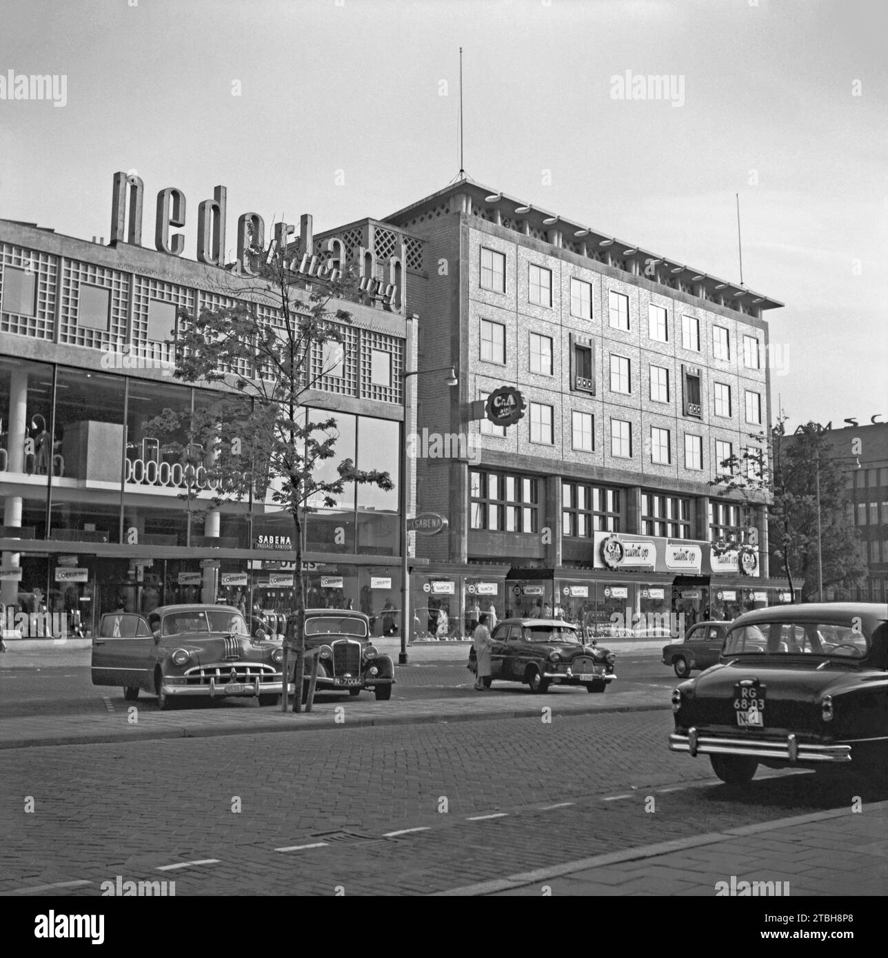 1955 ein Straßenblick von Rotterdam – fotografiert mit Blick über Beursplein in der Nähe der Kreuzung mit Coolsingel (rechts). Die geparkten Autos gehören der Vergangenheit an, Beursplein ist heute mit einem Einkaufszentrum und einer U-Bahn-Station unter dem Boden zu Fuß erreichbar. An der Ecke befindet sich ein C&A Bekleidungsgeschäft (heute stark modernisiert). Neonschilder an einem Gebäude zeigen „Nederland“ und „Kattenburg“ (eine Regenbekleidungsmarke) – ein Vintage-Foto aus den 1950er Jahren. Stockfoto