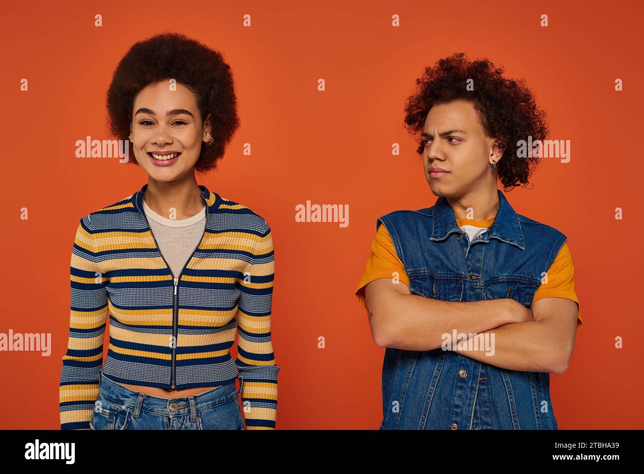 Junger afroamerikanischer Mann, der unzufrieden aussieht, während die Schwester fröhlich vor orangefarbenem Hintergrund lächelt Stockfoto