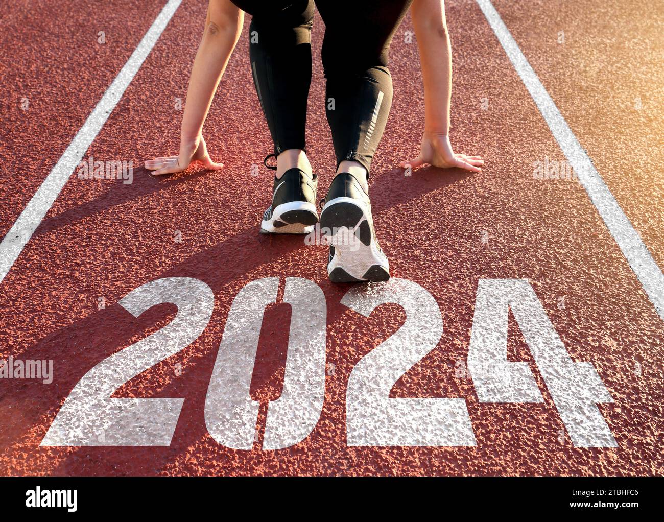 Rückansicht einer Frau, die sich auf eine Leichtathletikbahn vorbereitet, mit Gravur des Jahres 2024 Stockfoto