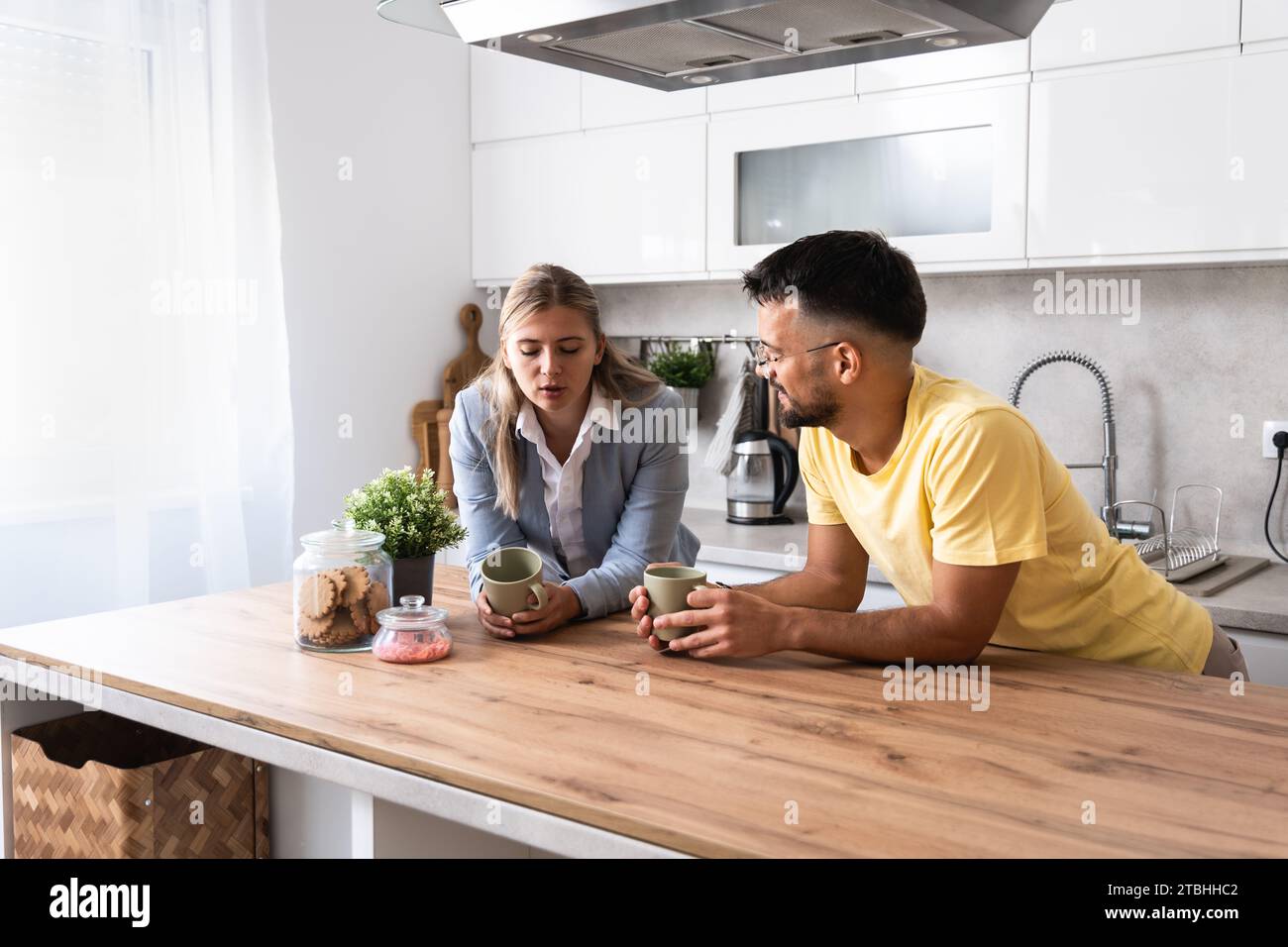 Kleine Gespräche. Mann und Frau stehen in der Küche und plaudern, während sie Kaffee trinken, nachdem die Frau von ihrem Arbeitsplatz nach Hause zurückgekommen ist. Businesswom Stockfoto