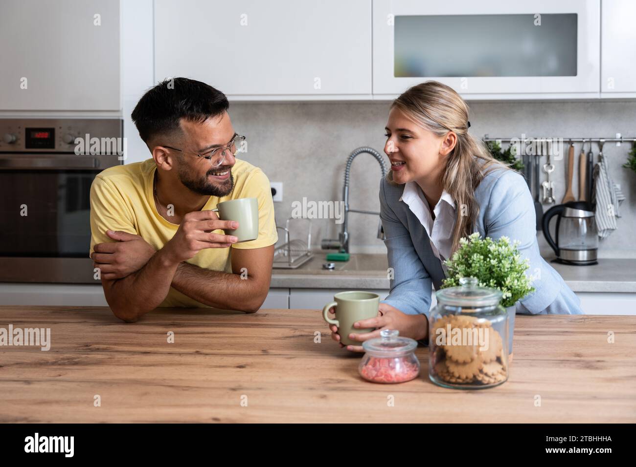 Kleine Gespräche. Mann und Frau stehen in der Küche und plaudern, während sie Kaffee trinken, nachdem die Frau von ihrem Arbeitsplatz nach Hause zurückgekommen ist. Businesswom Stockfoto