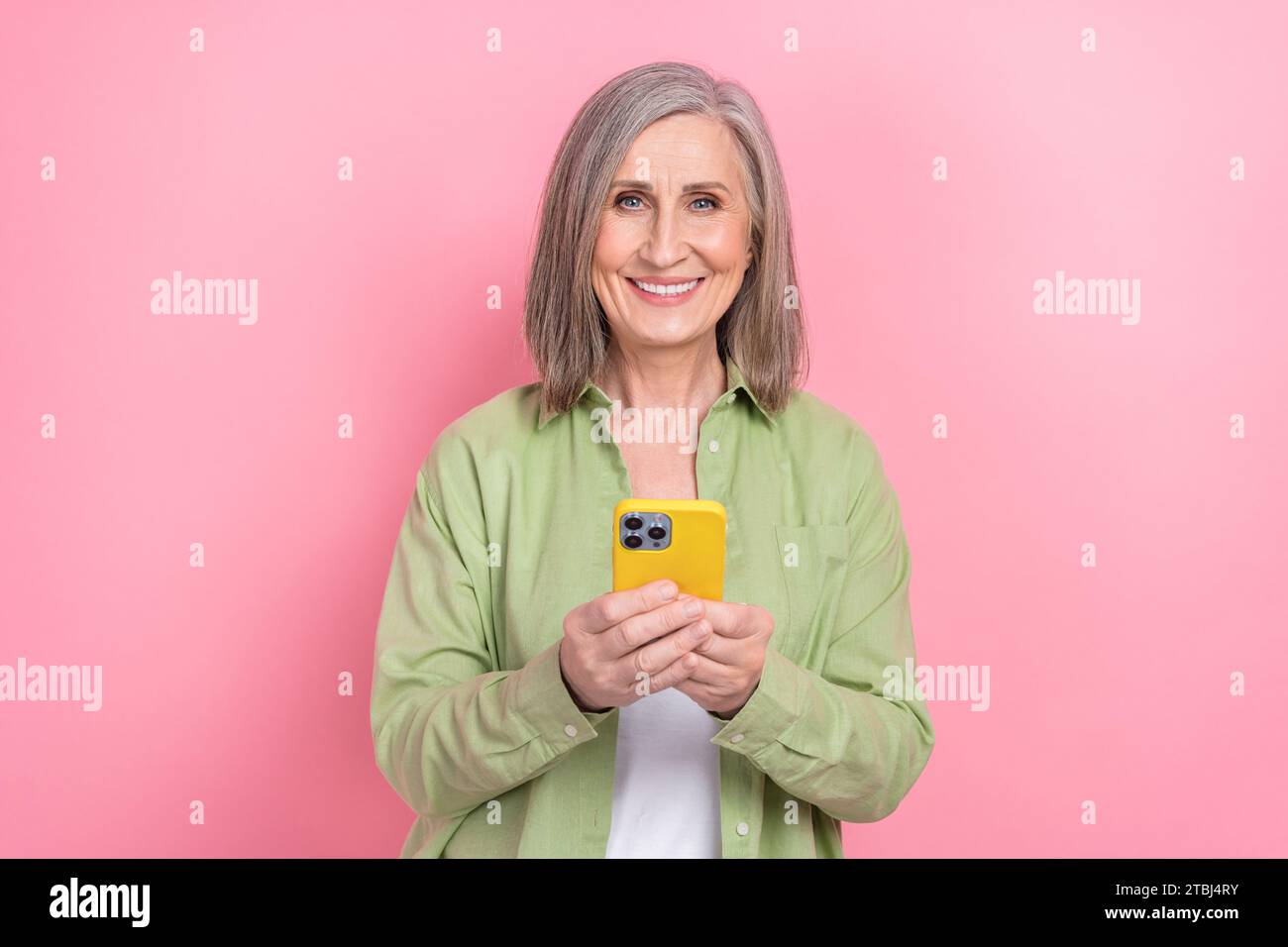 Porträt der charmanten Rentnerin Frau tragen khaki stilvolles Hemd Verwenden Sie gelben Fall Apfel iphone Kundenbewertung isoliert auf rosa Farbe Hintergrund Stockfoto