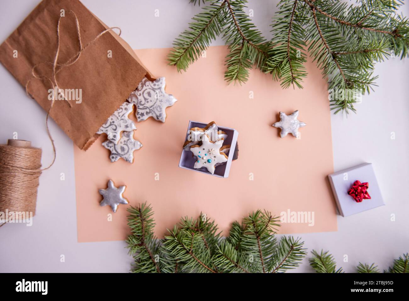 Auf Pfirsichfuzz isoliertem Hintergrund liegen Bastelbeutel mit silbernen Lebkuchenkeksen in Form von Schneeflocke für Weihnachten. Blick von oben auf das Stillleben mit Grün Stockfoto