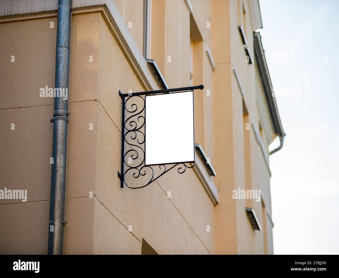 Leeres Vintage-Ladenschild an einem Gebäude. Leerer Kopierbereich zum Einfügen eines Logos oder der Öffnungszeiten. Stahlrahmen mit Ornamenten im Design montiert. Stockfoto