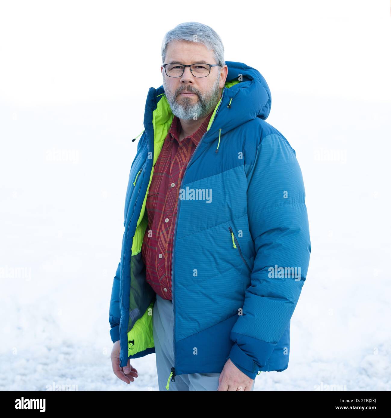 Mann, 56 Jahre, graues Haar und Bart, im Winter draußen mit Schnee im Hintergrund, dicke Daunenjacke Stockfoto