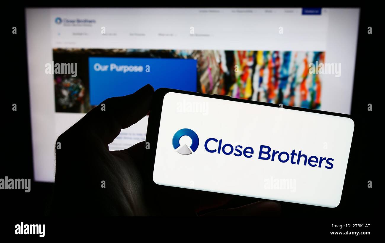 Person mit Smartphone und Logo der britischen Handelsbank Close Brothers Group plc vor der Website. Schwerpunkt auf dem Display des Telefons. Stockfoto